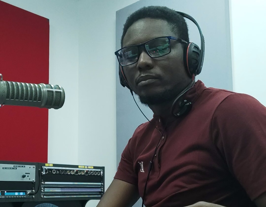 Kunle in red shirt with headphones on and a microphone in front of him